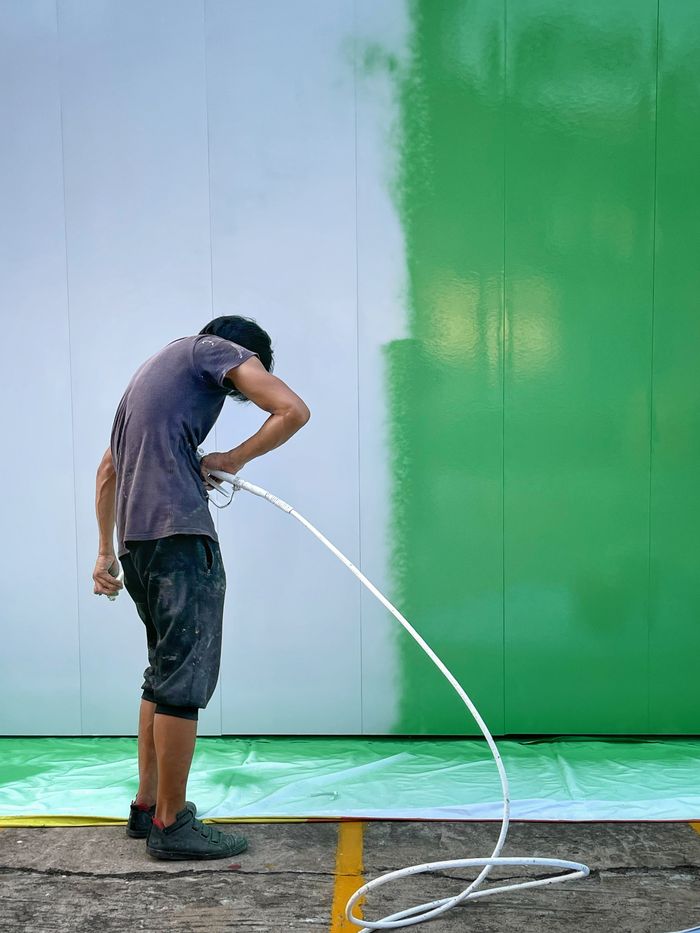 Hizmetlerimiz Man painting a large wall with a sprayer, transitioning from white to green.