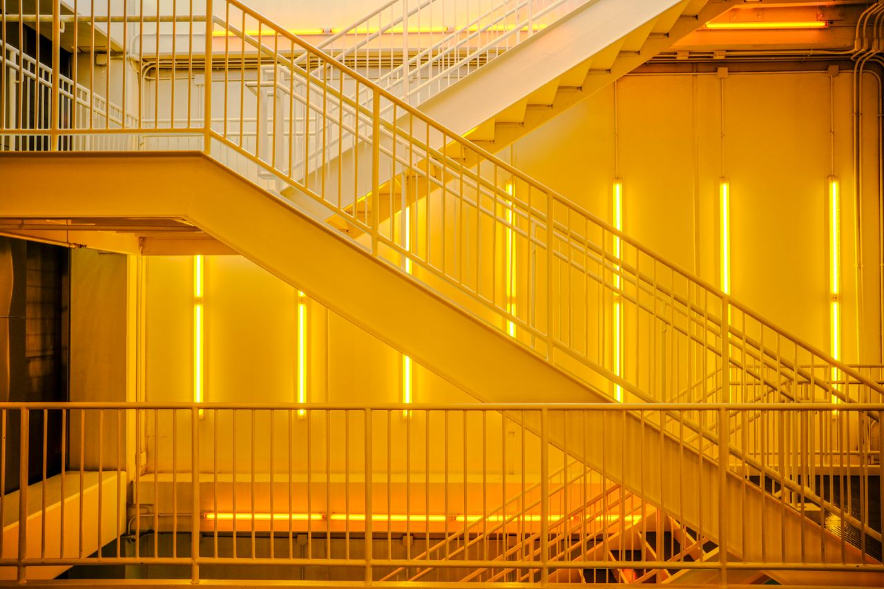 Hizmetlerimiz A contemporary staircase with bright yellow neon lights creating an industrial ambiance.