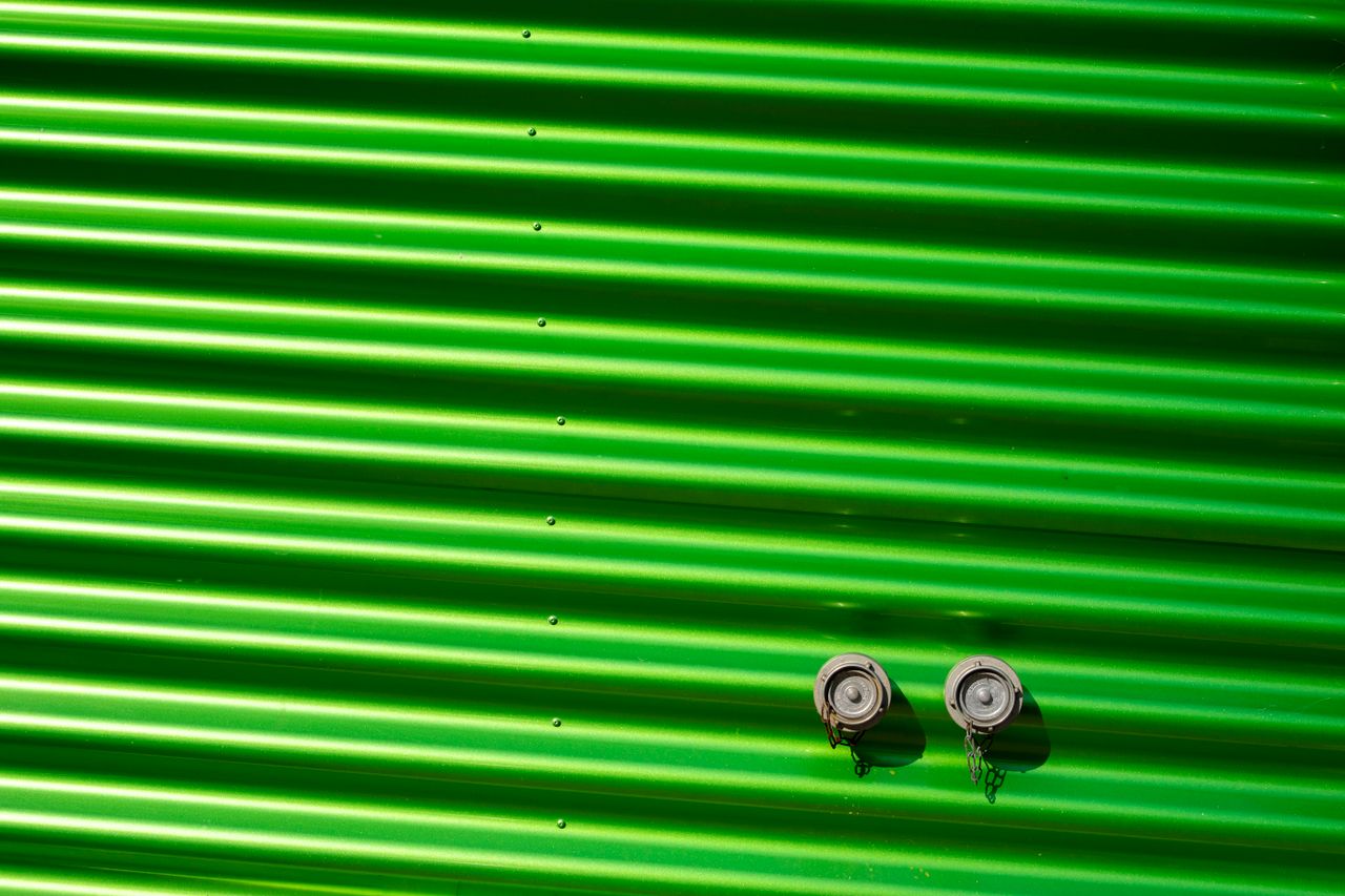 Hizmetlerimiz Close-up of a bright green corrugated metal wall featuring two metal bolts, showcasing industrial design.