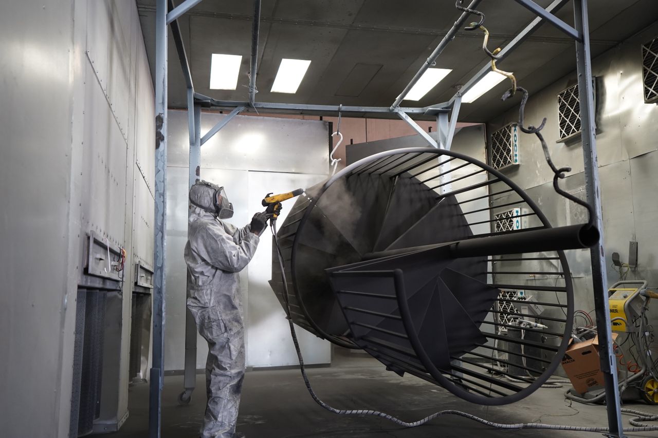 Anasayfa Technician performing powder coating on metal structure in industrial workshop.