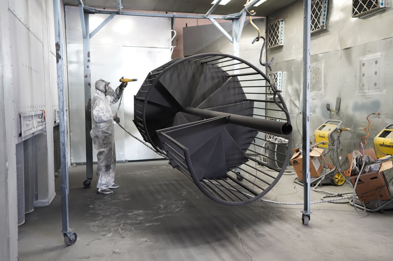 Anasayfa A worker in protective gear spray paints a large industrial metal structure indoors.