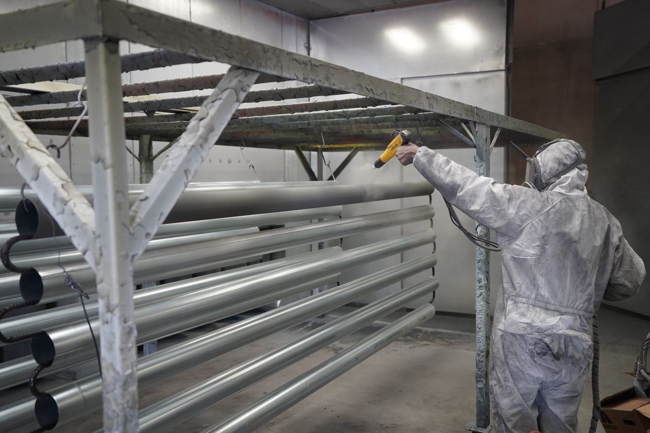 Anasayfa Technician applying powder coating to metal pipes in a workshop setting.