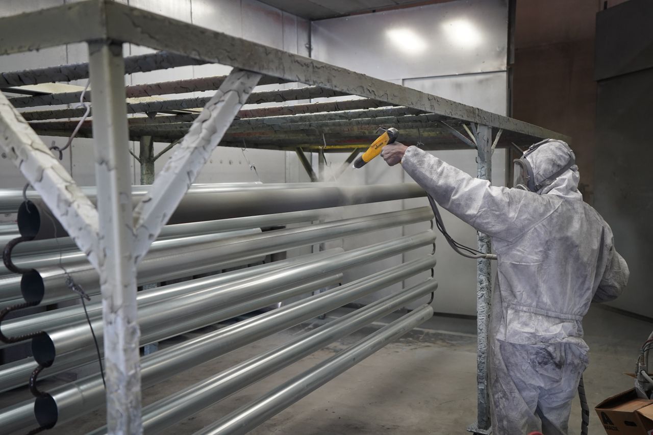 Portfolio Worker in protective gear applying powder coating to metal pipes in a factory setting.