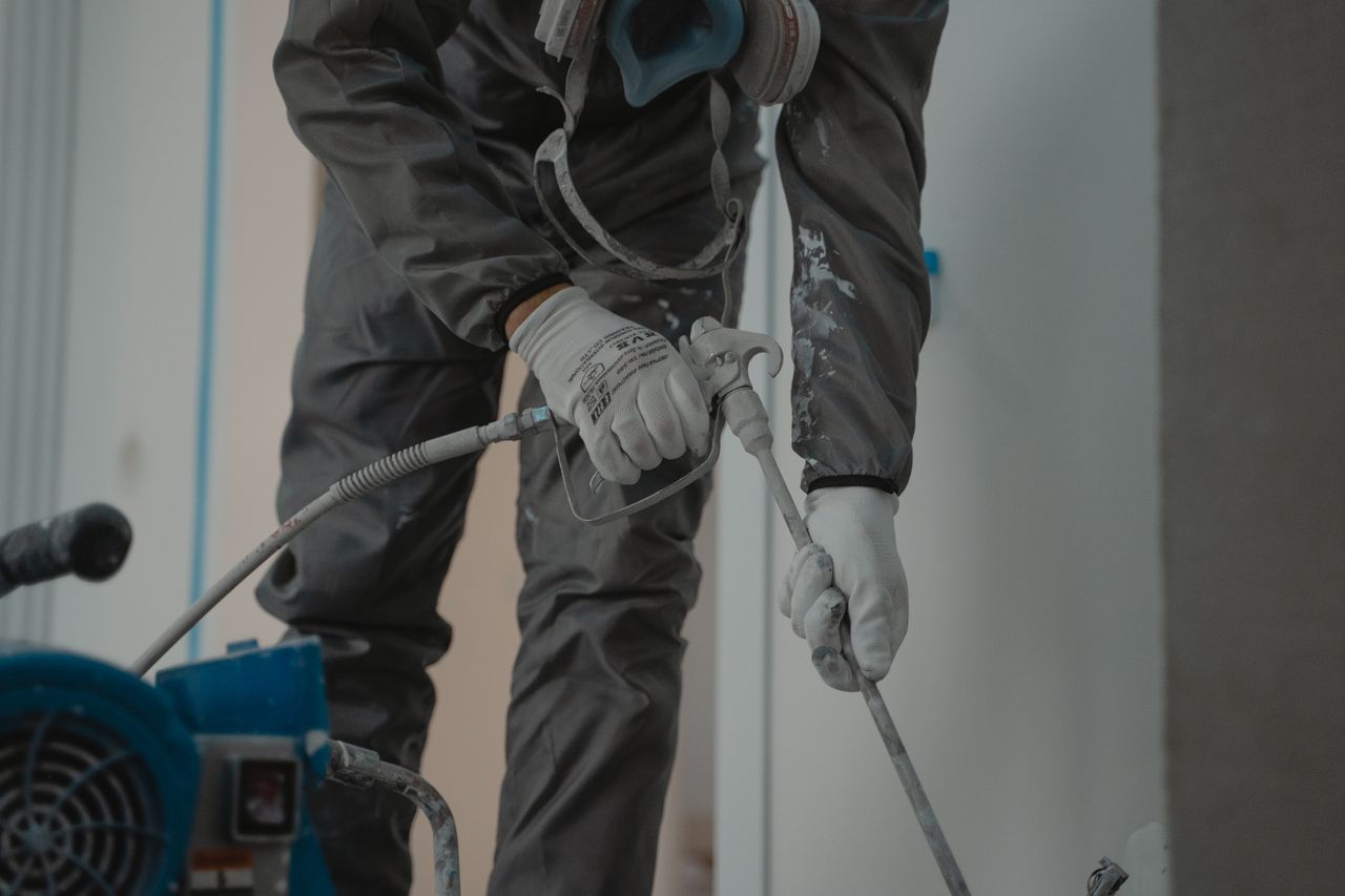 Portfolio Worker in protective gear using a power spray for indoor renovation.